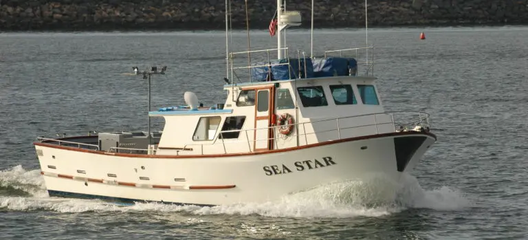 A white boat named "Sea Star" navigates through water near a rocky breakwater, with small waves forming at its bow.